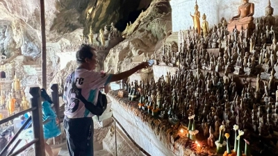 Ein Mann besprenkelt Buddha-Statuen in den Pak Ou Caves als Zeichen des tiefen Respekts mit Wasser. (Foto: Carola Frentzen/dpa)