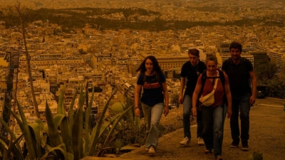 Touristen spazieren auf dem Lycabettus-Hügel, während der Himmel über Athen mit dem antiken Akropolis-Hügel im Hintergrund infolge von Saharastaub eingetrübt ist. (Foto: Petros Giannakouris/AP/dpa)